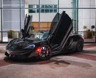 McLaren 570S Spider — Black, front three-quarter view with doors raised